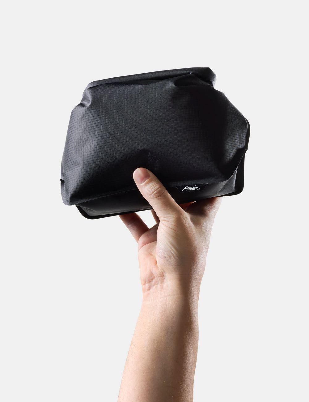 Matador FlatPak Waterproof Toiletry Case (V2) in Black - hand holding a Black toiletry case on a light gray background