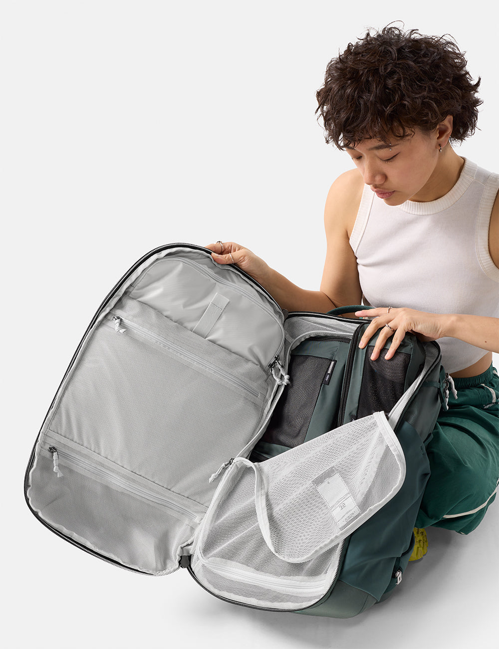Matador 35L Global Travel Pack in Juniper - person organizing a green backpack with multiple compartments on a white background