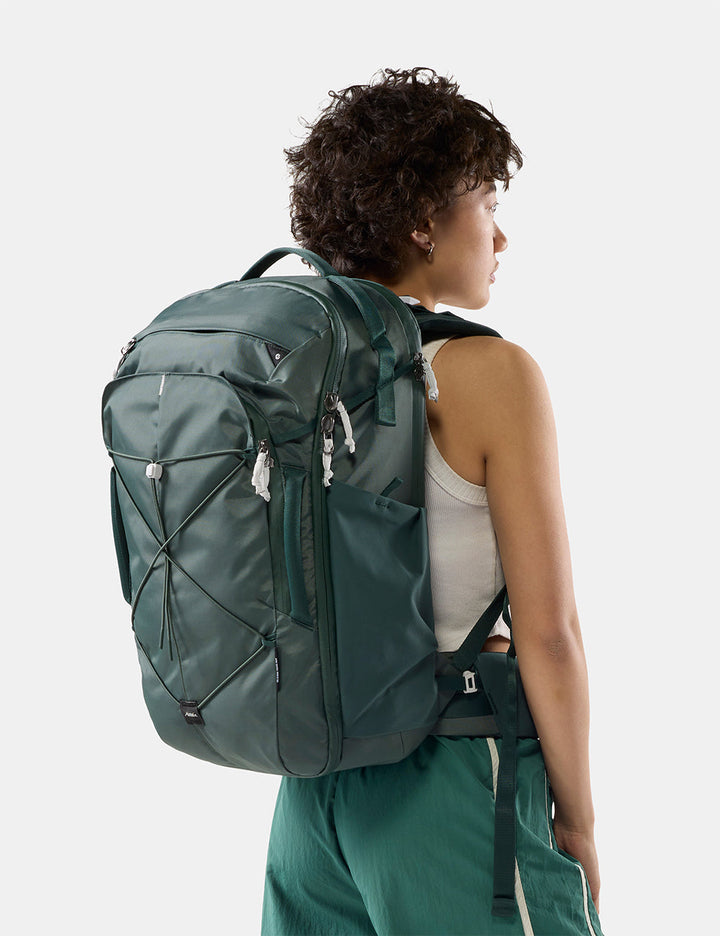 Matador 35L Global Travel Pack in Juniper - a woman shown from the back wearing a dark green technical backpack, set against a plain light gray studio background