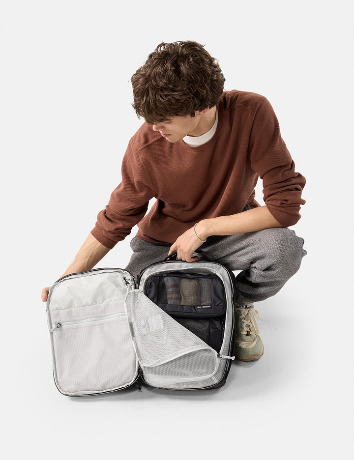 Matador 18L Personal Item Travel Pack in Black - person unpacking a travel bag on a white background