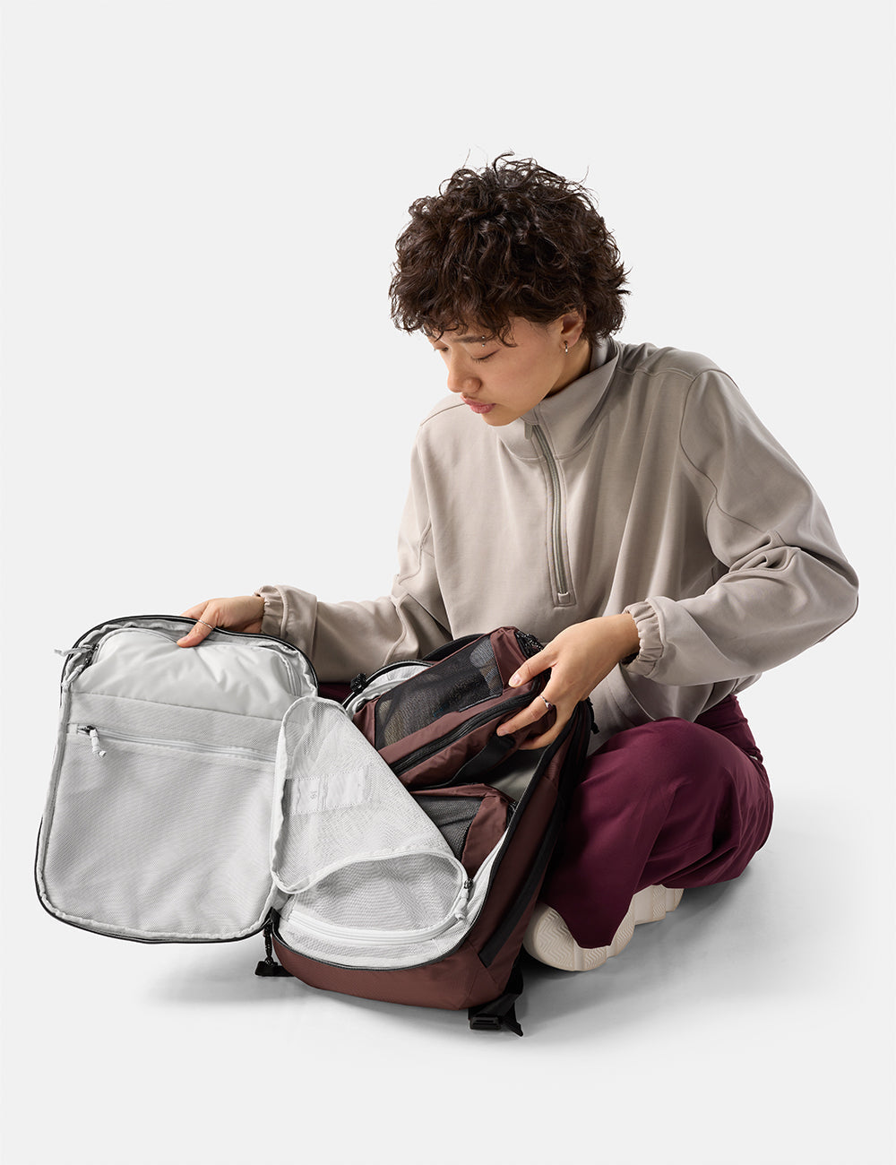 Matador 18L Personal Item Travel Pack in Garnet - person organizing a garnet backpack on a white background