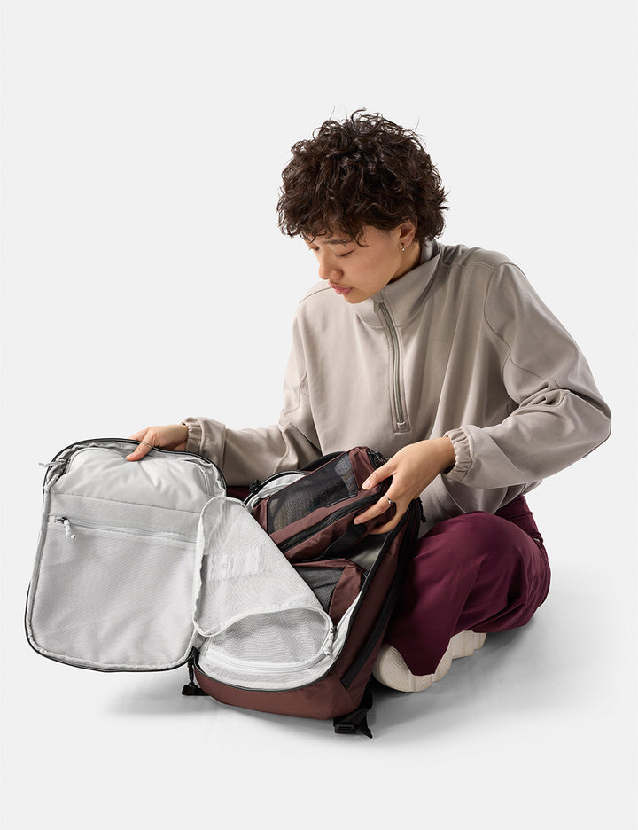 Matador 18L Personal Item Travel Pack in Garnet - person organizing a garnet backpack on a white background