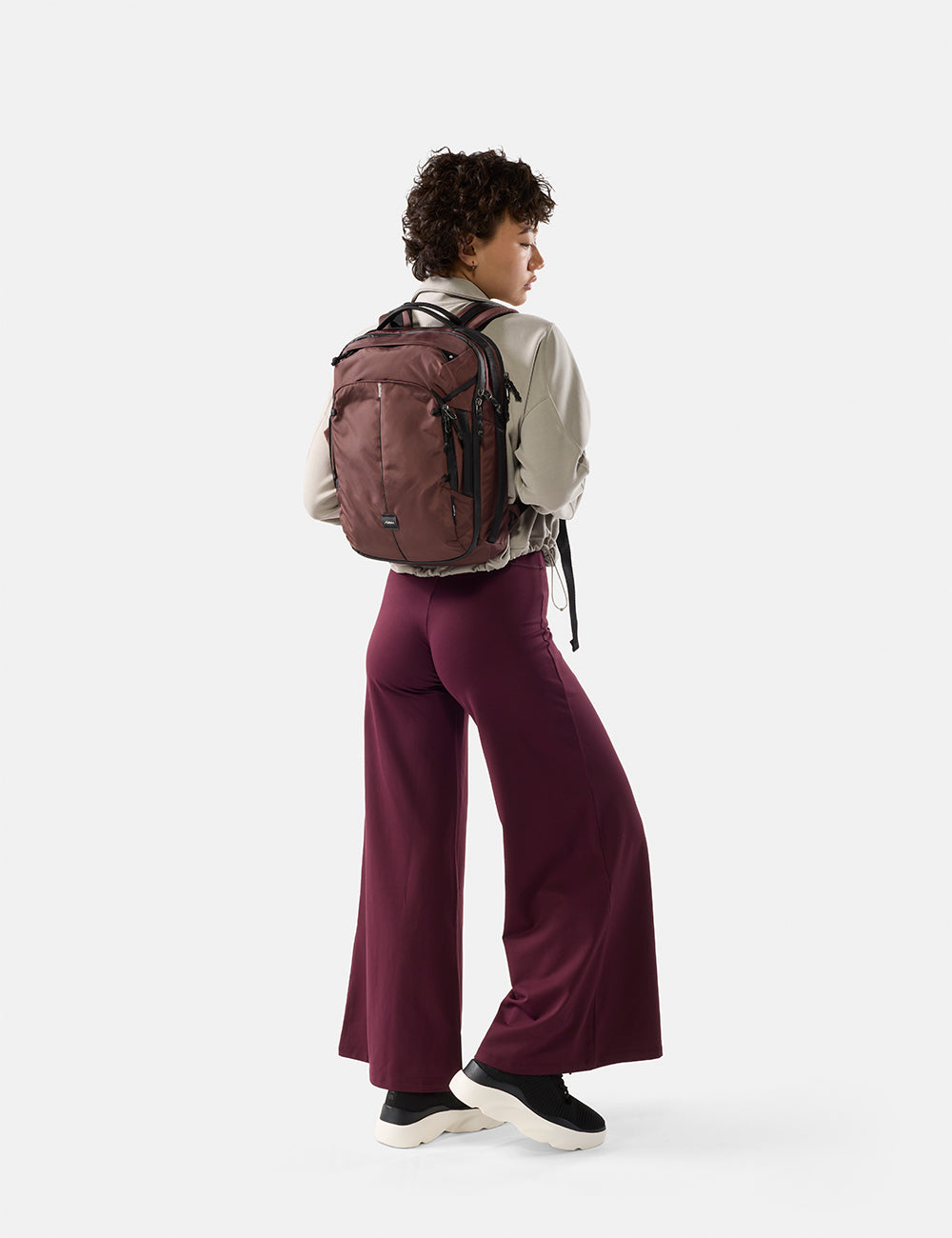 Matador 18L Personal Item Travel Pack in Garnet - person wearing a garnet backpack and garnet pants on a white background