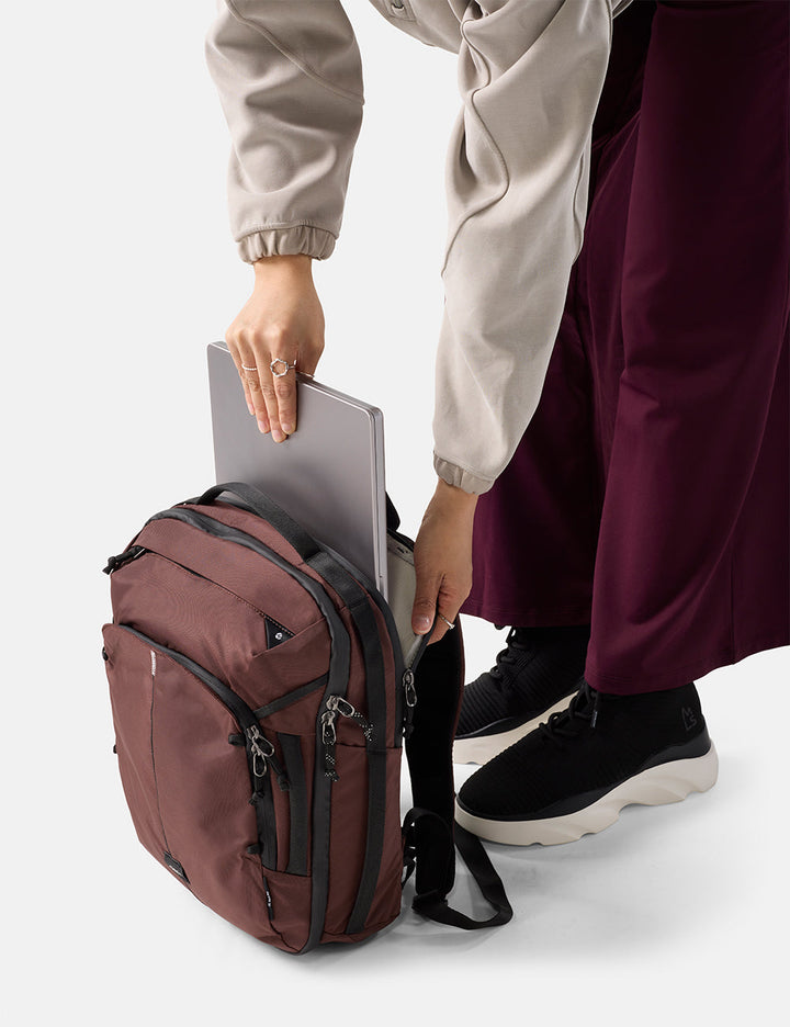 Matador 18L Personal Item Travel Pack in Garnet - person holding a laptop in a maroon backpack on a white background