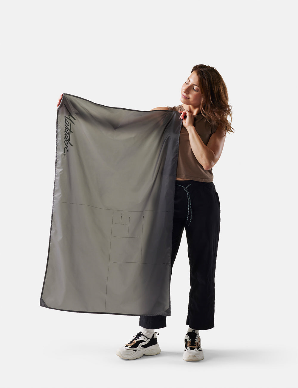 Matador Mini Pocket Blanket™ 4.0 - 110 x 70cm in Black - person holding a large gray fabric with a brand logo on a white background