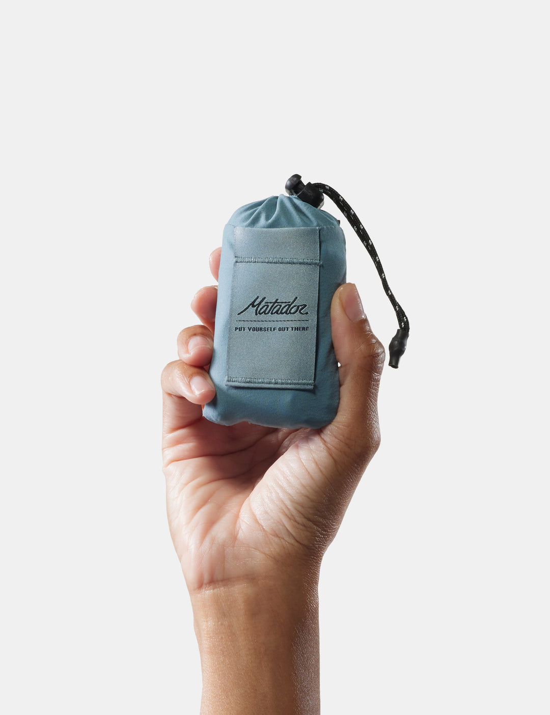 Matador Mini Pocket Blanket™ 4.0 - 110 x 70cm in Blue - hand holding a small blue drawstring bag with &