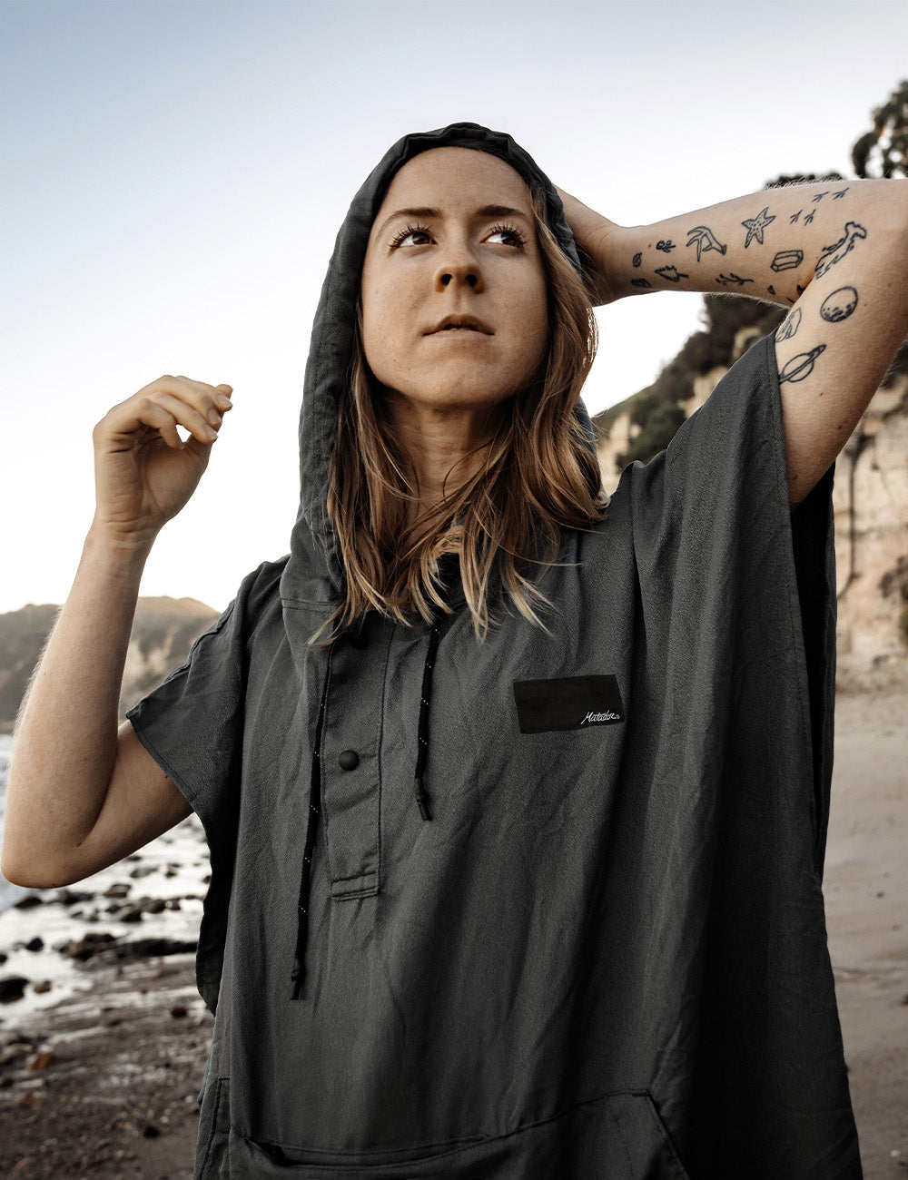 Matador NanoDry™ Packable Towel Poncho in Charcoal - person wearing a gray poncho with a brand logo on a beach