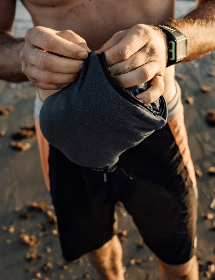 Matador NanoDry™ Packable Towel Poncho in Slate Blue - person on a beach holding a black pouch with a watch on their wrist