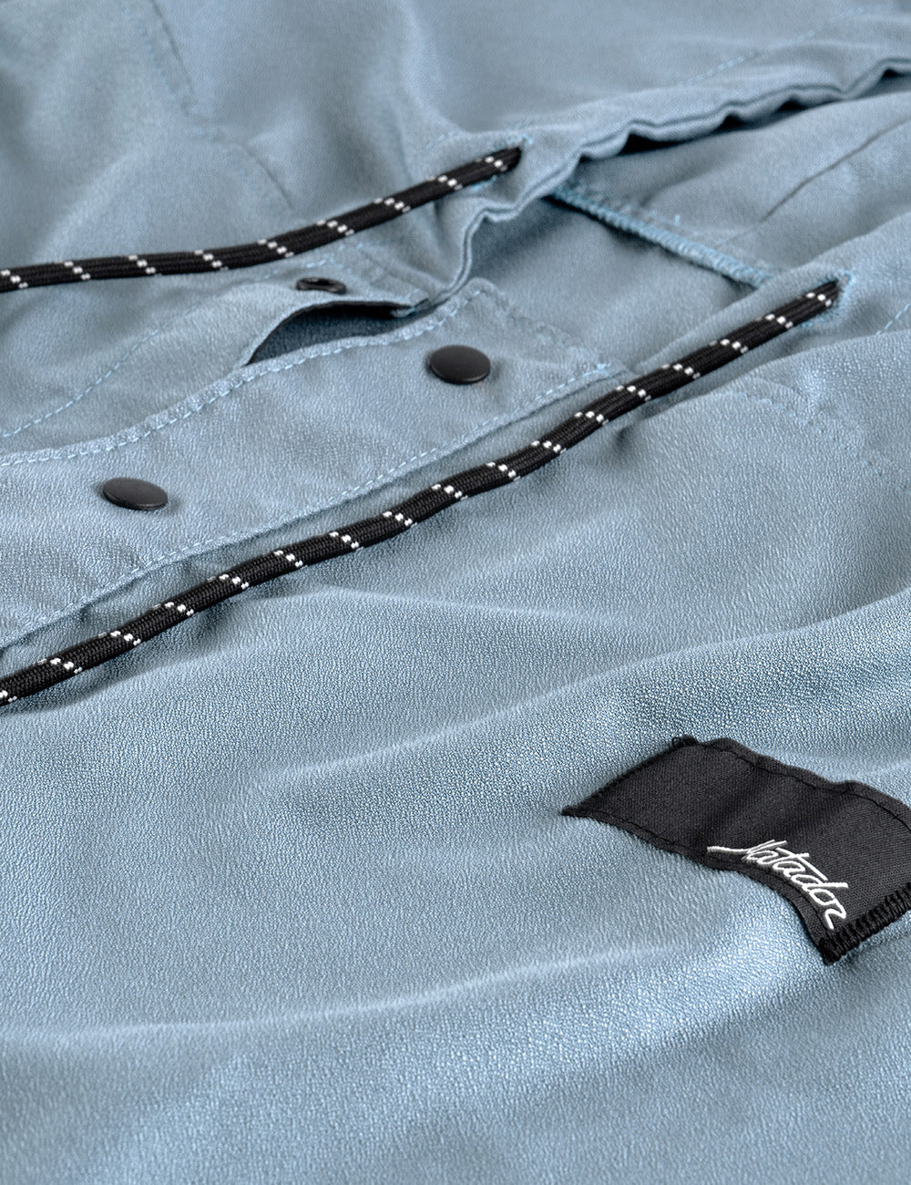 Matador NanoDry™ Packable Towel Poncho in Slate Blue - close-up of a light blue poncho with a brand label on a textured fabric background